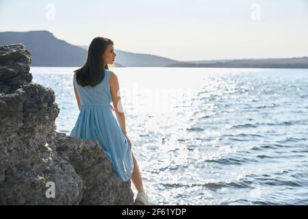 Attraente donna dai capelli scuri in un abito elegante seduta sulla pietra nella baia di Bakota. Felice donna trascorrere del tempo libero su bella natura. Vista panoramica del fiume Dniester. Foto Stock