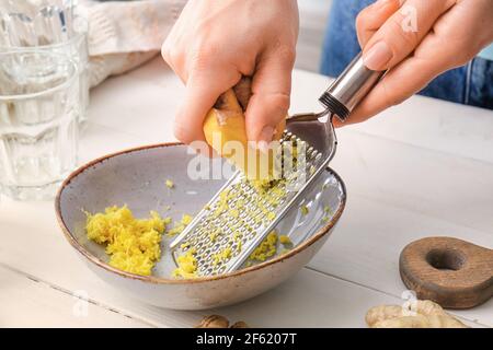 Donna grattugiare zenzero su sfondo bianco di legno Foto Stock