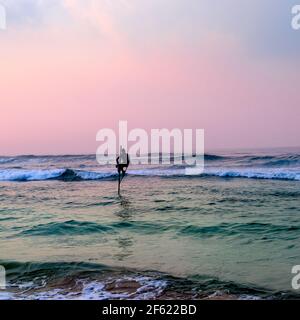 Silhouette dei tradizionali pescatori a palafitte al tramonto vicino a Galle in Sri Lanka. Foto Stock