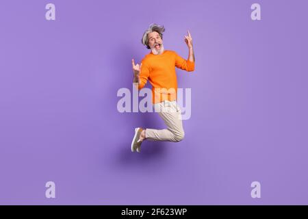 Foto a dimensione intera di giovane pazzo funky divertente sorridente vecchio uomo che salta mostrando rock'n'roll segno isolato su sfondo di colore viola Foto Stock