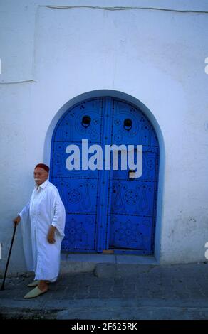 Tunisino indossando un tradizionale Djellaba bianco vicino ad una porta blu, Sidi Bou ha detto, Tunisia Foto Stock