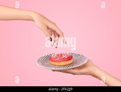 La mano delle donne prende la ciambella gustosa su sfondo rosa. Modello mockup per panetteria Foto Stock