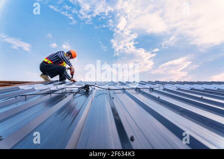 Concetto di costruzione del tetto, Roofer con pistola pneumatica o pneumatica per chiodi e installazione su nuova lamiera del tetto. Foto Stock