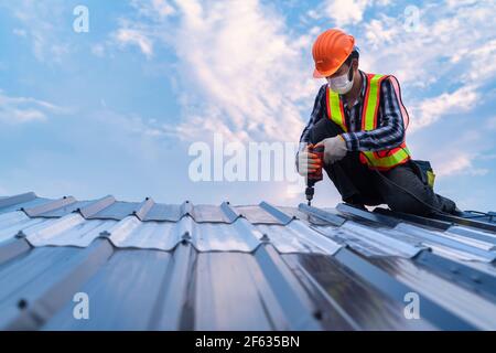 Copertura che lavora sulla struttura del tetto dell'edificio in cantiere, Roofer con pistola pneumatica o pneumatica per chiodi e installazione su nuova lamiera del tetto. Foto Stock