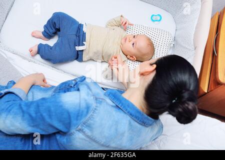 la madre gioca con un bambino che sta mentendo in a. letto laterale per un neonato o in un moderno box Foto Stock