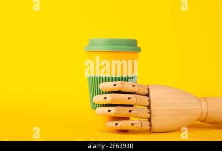 Manichino in legno che tiene la tazza da caffè riutilizzabile su una tazza gialla sfondo con spazio per il testo Foto Stock