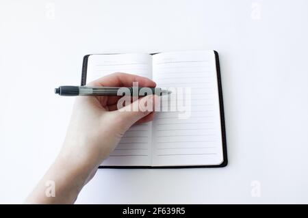 La mano della donna sta scrivendo su un notebook con una penna su sfondo bianco. Vista dall'alto Foto Stock