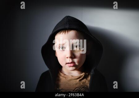 Povero ragazzo triste con sopracciglia tagliata in piedi in casa, concetto di povertà. Foto Stock