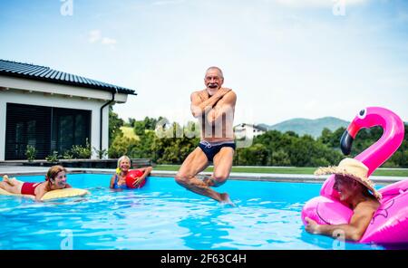 Gruppo di anziani allegri in piscina all'aperto in cortile, saltando. Foto Stock