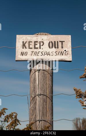 Un cartello di avvertimento su un palo di legno recita tenere fuori - Nessun Trespassing Foto Stock