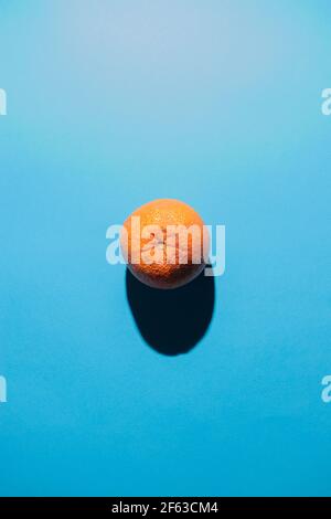 Un arancione centrato nella foto con un'ombra allungata su uno sfondo blu. Foto Stock