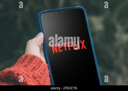 Logo Netflix su uno smartphone, fornitore globale di film in streaming e serie TV. Donna che guarda il video dal servizio Netflix su smartphone Foto Stock