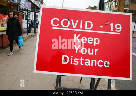 Una donna cammina oltre un cartello con la scritta 'COVID-19, Keep your distance' a Londra. Foto Stock