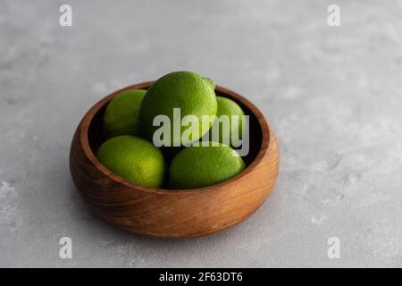Ciotola in legno riempita con Limes verde brillante su superficie grigia Foto Stock