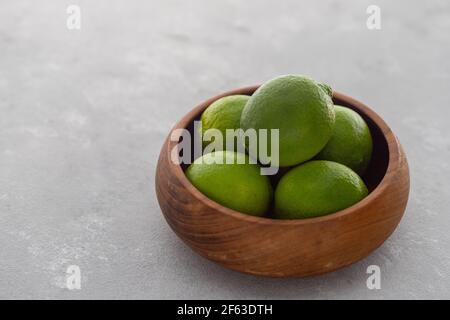 Lime verde brillante in ciotola di legno su superficie grigia Foto Stock