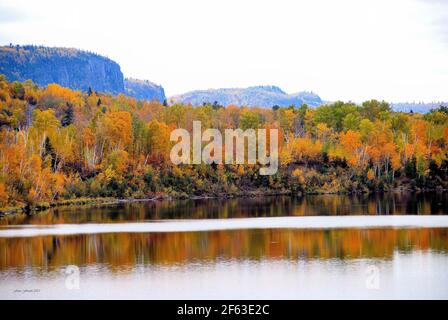 Il fiume Kaministiqua riflette il fogliame vivido sulla riva, mentre la catena montuosa del Nord Ovest è vista sullo sfondo in una giornata nuvolosa. Foto Stock