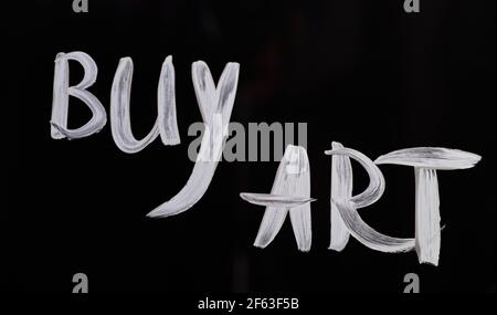 Una mano che scrive su vetro 'Buy Art'. Testo del messaggio per costringere le persone ad acquistare arte online o offline. Sfondo nero. Foto di alta qualità Foto Stock