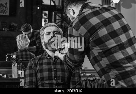 Ritratto di mascolinità. Master barbiere fa la acconciatura e styling con asciugacapelli. Barbiere. Giovane hipster con barba che taglia i capelli in un Foto Stock