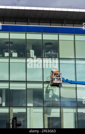 Pulitori per finestre con piattaforma di raccolta dei ciliegi per lavare i finestrini di un ufficio. Lavoratori che utilizzano una piattaforma di lavoro aerea per accedere all'edificio alto. Asta alimentata ad acqua Foto Stock