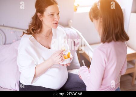 Attenta giovane donna incinta che mangia insalata di frutta con la sua bambina. Foto Stock