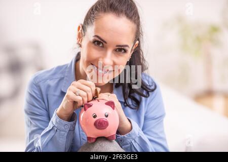 Bella donna risparmia denaro mettendo le monete in una banca piggy. Foto Stock