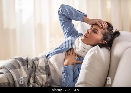 La donna soffre di sintomi come dolore ai polmoni e mal di testa mentre si riposa sul divano a casa. Foto Stock