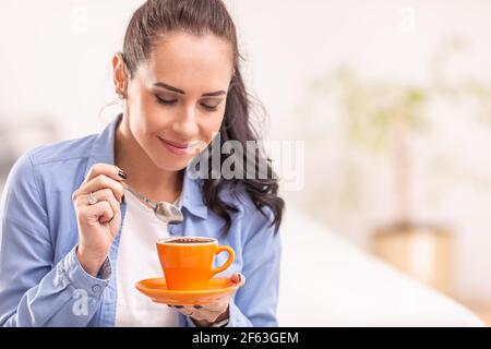 Bella donna odore di caffè fresco da una tazza arancione. Foto Stock