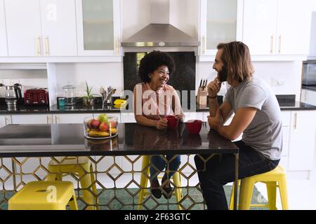Felice coppia diversa seduta in cucina bere caffè e parlare Foto Stock