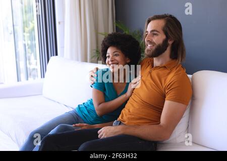 Felice coppia diversa seduta sul divano abbracciando e sorridendo Foto Stock
