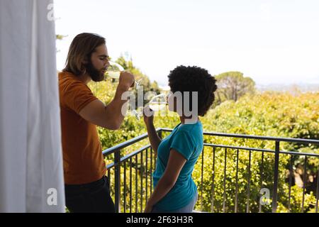 Felice coppia diversa in piedi sul balcone bere vino Foto Stock