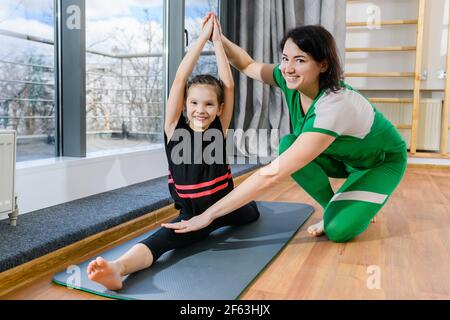 L'istruttore della donna aiuta la ragazza del bambino di pre-teen con gli esercizi di workout di stretching al tappetino di sport all'interno, infanzia sana Foto Stock