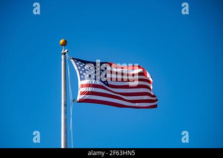 Una bandiera americana sventolando nella brezza contro una chiara cielo blu Foto Stock