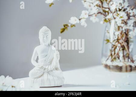 Statuetta decorativa bianca di Buddha con rami di alberi sanguinanti nel vaso su sfondo bianco. Rituale di meditazione e relax. Compleanno Buddha Foto Stock