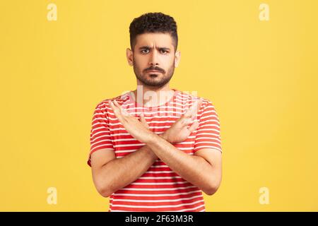 Non c’è modo. Interessato uomo bearded in t-shirt a righe che attraversa le mani mostrando x gesto, rifiutando bullismo e abuso seriamente guardando la fotocamera. Foto Stock