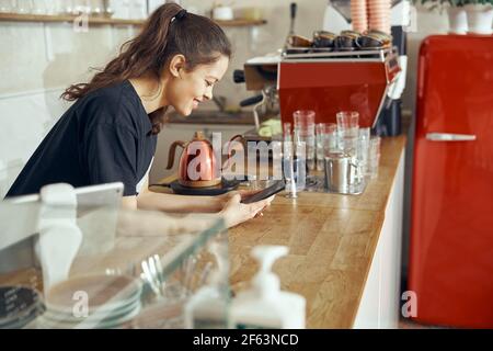 Barista che effettua l'ordine dal cliente online sullo smartphone. Concetto di caffetteria e caffetteria per piccole imprese Foto Stock