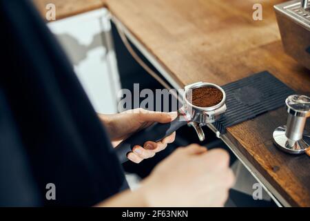 Barista che tiene il supporto per il caffè premendo il caffè nel supporto per la macchina da caffè, primo piano Foto Stock