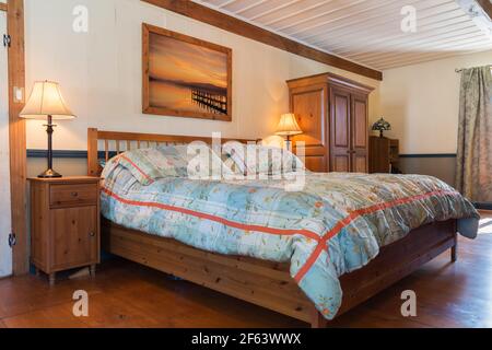 Letto king size su struttura in legno con testiera in legno, comodino in legno di pino colorato scuro e armadio nella camera da letto principale all'interno di una vecchia casa del 1825 Foto Stock