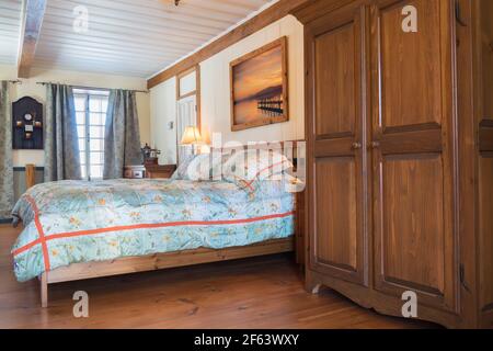 Letto king size su struttura in legno con testiera in legno e. grande armadio in legno di pino colorato scuro nella camera da letto principale all'interno Una vecchia casa Canadiana del 1825 Foto Stock