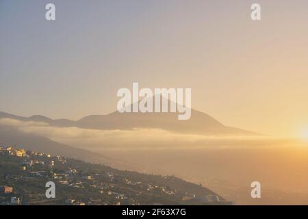 Vista di Teide al tramonto con foschia con un villaggio sulla collina. Foto Stock