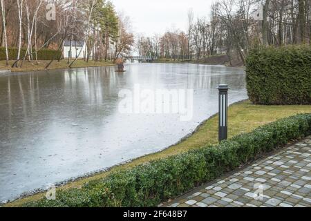 Vista sul lago invernale coperto di ghiaccio nel parco. Foto Stock