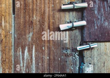 Tre piccoli rotoli di carta bianca di notifica inseriti in vecchio lucchetto arrugginito sulla vecchia porta di legno. Bollettino che si stacca al cancello della a Foto Stock