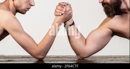 Due mani di uomo hanno stretto il braccio wrestling, forte e debole, corrispondenza disuguale. Braccio uomo pesante muscled bearded wrestling un uomo debole puny. Bracci di lotta sottili Foto Stock