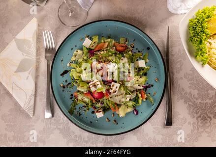 Pranzo con dieta colorata, insalata di primavera. Foglie fresche, rafano, formaggio feta e olio d'oliva in un piatto blu Foto Stock
