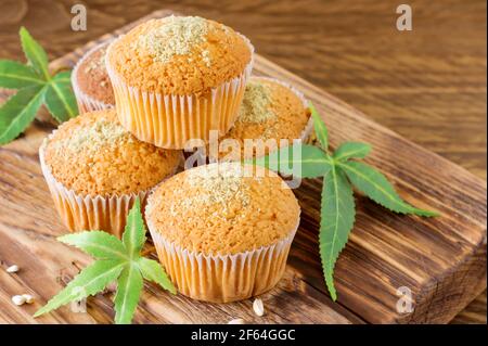 Muffin sani e gustosi privi di glutine e vegani con semi di canapa su una scrivania in legno da vicino. Muffin alla tazza di marijuana con foglie di cannabis. Foto Stock