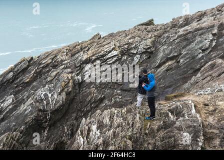 Due turisti che usano il loro smartphone per fotografare la vista dalle rocce di Towan Head a Newquay in Cornovaglia. Foto Stock