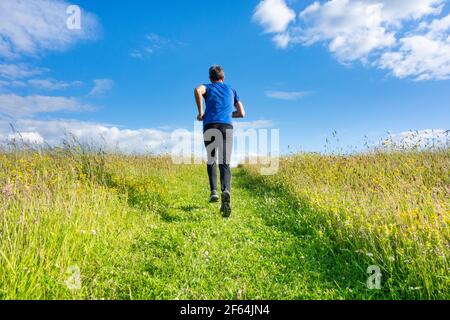 Vista posteriore di un uomo maturo che corre, jogging in salita su un sentiero in erba su una collina in campagna. REGNO UNITO Foto Stock