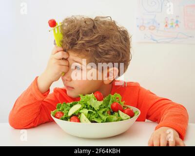 Ciotola con insalata di mais, lattuga di agnello, cetriolo e pomodori ciliegini. Carino ragazzino non vuole mangiare cibo sano. Foto Stock