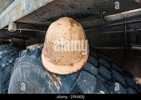 L'elmetto di sicurezza si trova sulla ruota del carrello. Elmetto sporco di un operaio di petrolio e gas. Sicurezza e tutela del lavoro dei geologi. Foto Stock