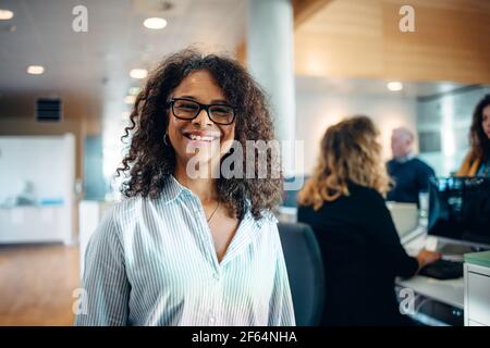 Ritratto di una donna di successo che lavora in ufficio comunale. Felice donna matura in piedi alla reception guardando la macchina fotografica e sorridente peop Foto Stock