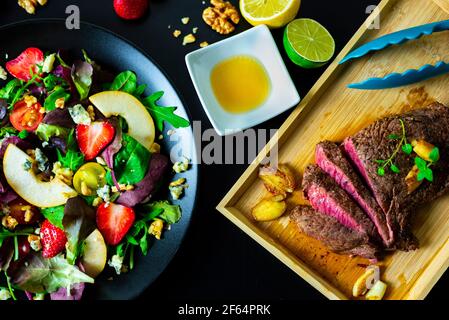 Bistecca tagliata con insalata mista con fragole, pere, noci, formaggio blu e salsa al miele di limone Foto Stock